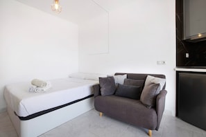 Une pièce de taille modeste comprenant un lit, un canapé, une petite table et un téléviseur encastré.