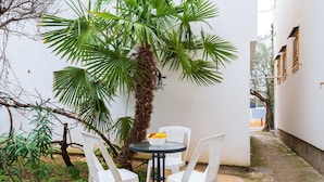 A small outdoor seating area with a round table and four white plastic chairs, surrounded by lush greenery including a palm tree. - Awesome apartment in Fazana (Fazana)