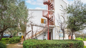 A building with a red spiral staircase leading to a balcony, surrounded by greenery and trees. - Awesome apartment in Fazana (Fazana)