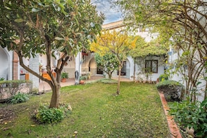 A courtyard with a small tree, a grassy area, and a building with white walls and a tiled roof. - Holiday Home "Carmen San Andrés" with Mountain View, Private Terrace & Wi-Fi (Granada)