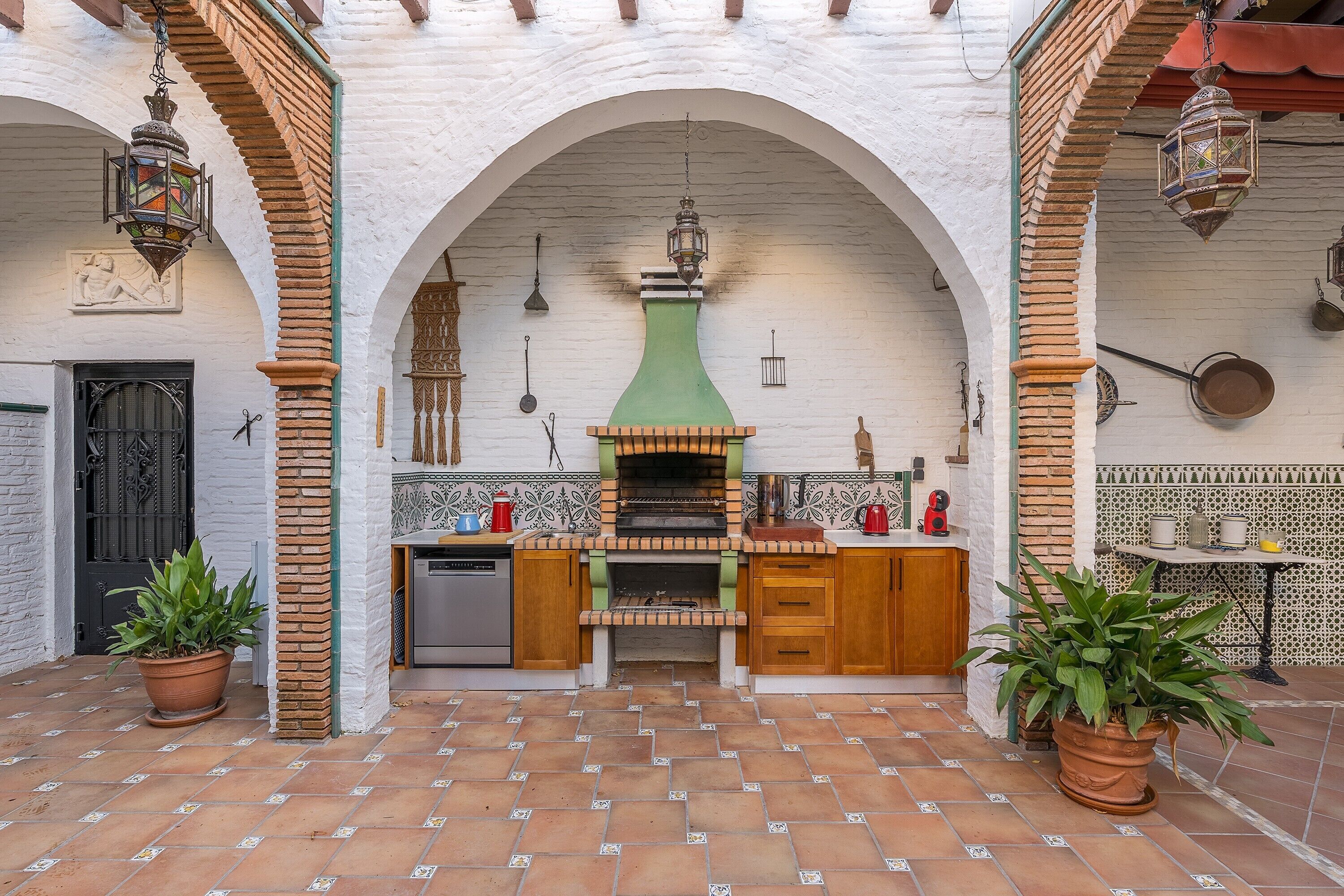A courtyard with a brick floor, a central oven, and potted plants.