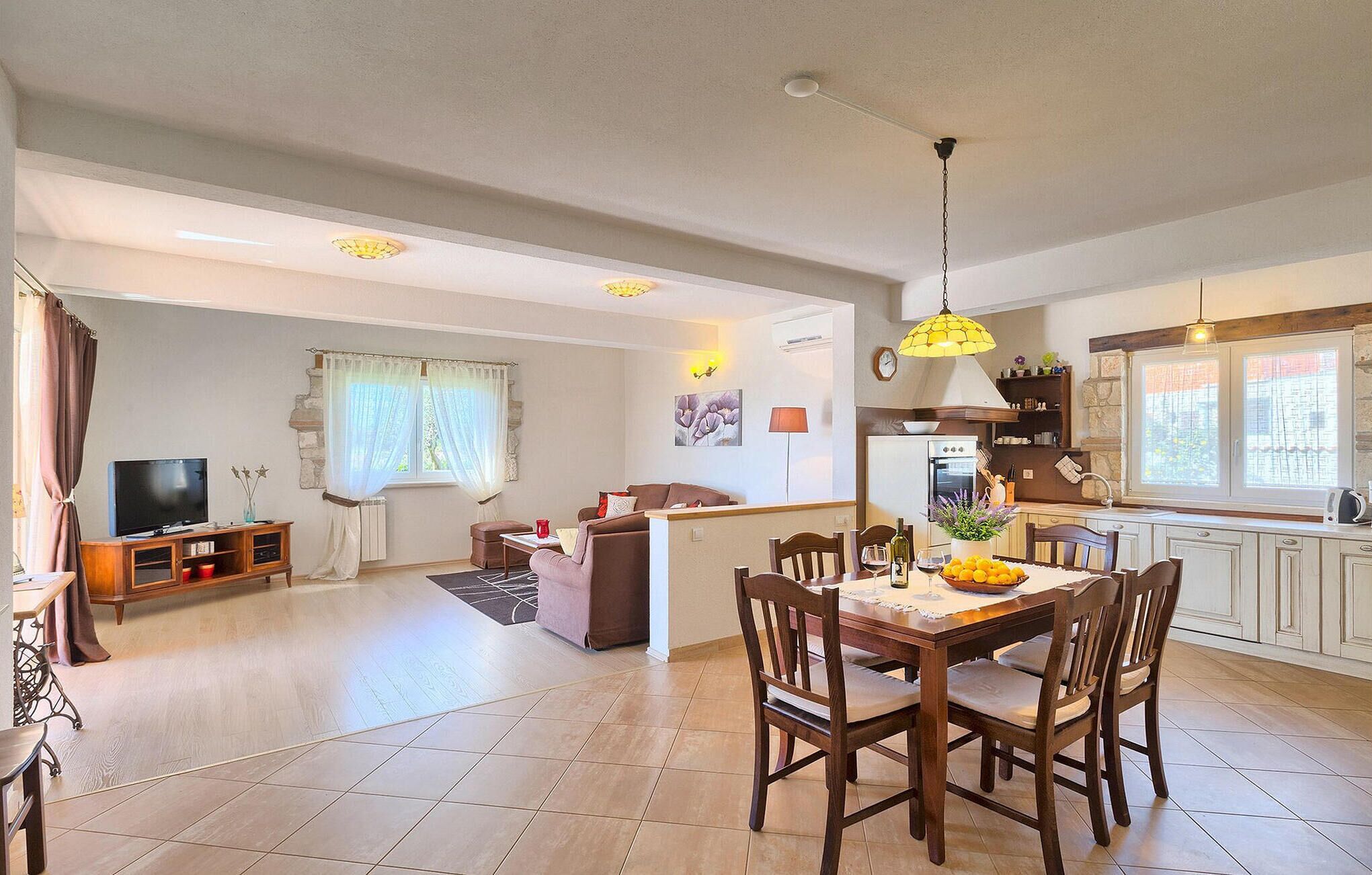 A spacious living area with a dining table, chairs, a TV, and a kitchen with a window.