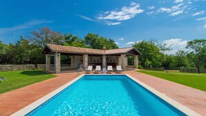 A rectangular swimming pool with a tiled deck surrounding it, a covered patio area with chairs, and a stone wall in the background. - Gorgeous home in Svetvincenat with WiFi (Svetvincenat)