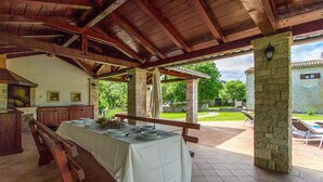 An outdoor dining area with a covered patio, stone pillars, and a view of the surrounding garden. - Gorgeous home in Svetvincenat with WiFi (Svetvincenat)