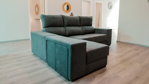 Ein modernes Wohnzimmer mit Ecksofa, Holzboden und minimalistischer Einrichtung.