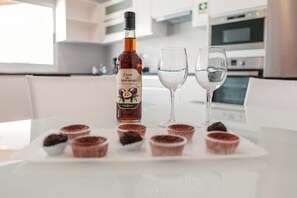 A bottle of liquor, two glasses, and several cupcakes on a table in a modern kitchen. - Casa Maresia - 5 mins from the sea (Fenais da Luz)