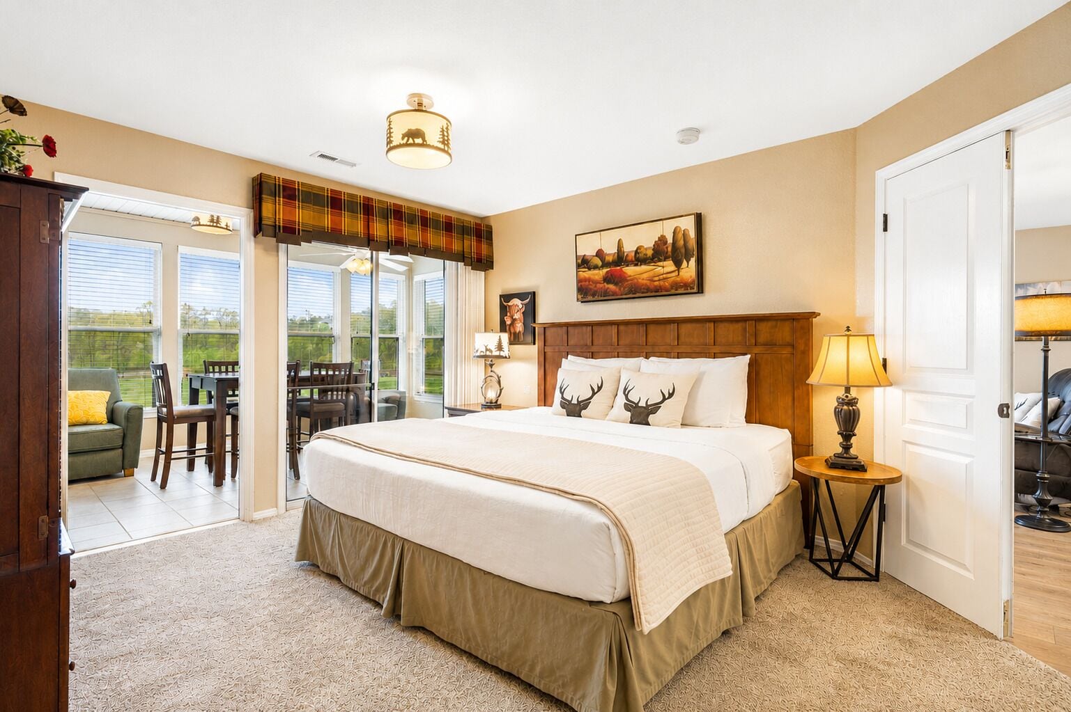A bedroom with a large bed, a wooden headboard, a painting, a lamp, and a view through a glass door.