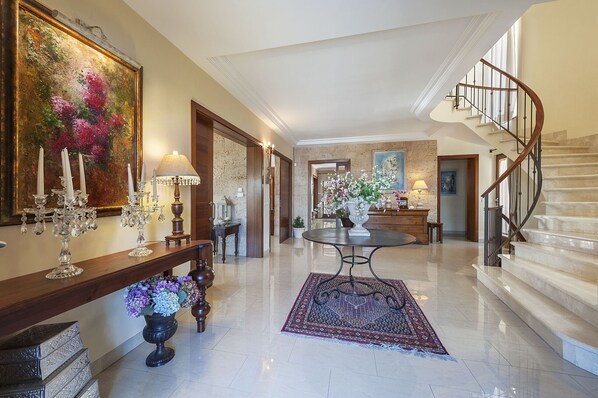 A spacious foyer with a marble floor, a grand staircase, and a large painting on the wall.