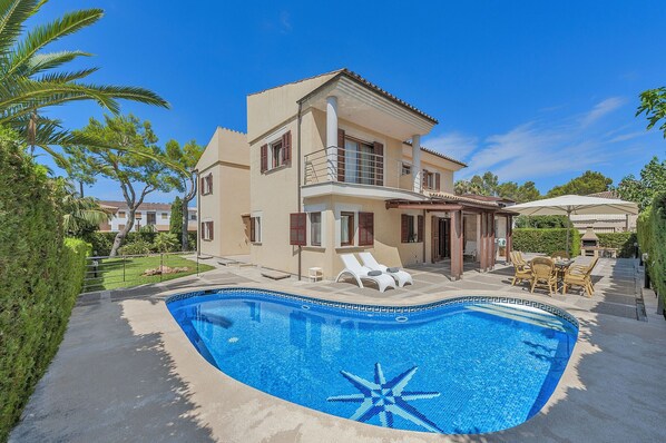 Une maison à deux étages avec une piscine, du mobilier d’extérieur et un jardin bien entretenu.
