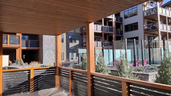 A modern multi-story building with balconies, a covered outdoor area with wooden railings, and a view of the surrounding landscape.