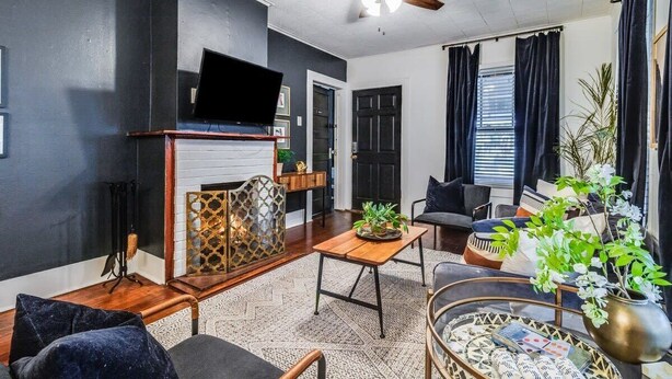 A living room with a fireplace, a ceiling fan, and a television. - 4BR Downtown Lafayette-Garden, Parking, Walk to Arts District (Lafayette)
