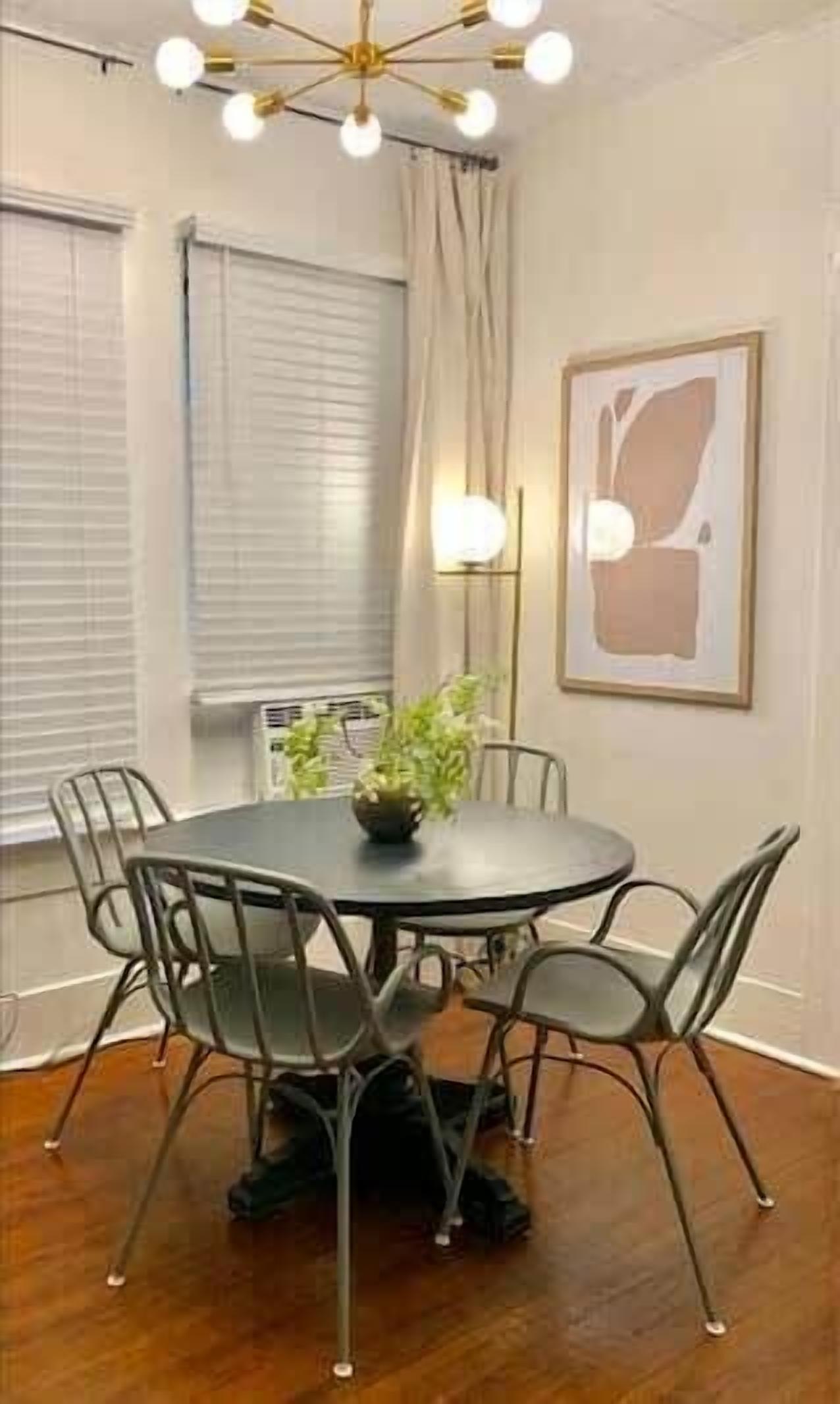 Una mesa de comedor redonda con seis sillas, una planta en maceta y un moderno candelabro arriba.