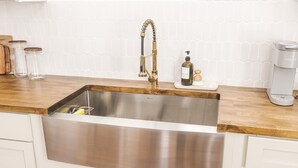 A kitchen with a stainless steel sink, wooden countertop, and white cabinetry. - Modern Art-Deco – Steps from Downtown Lafayette (Lafayette)