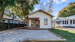 A single-story house with a porch, a flag, and a gravel driveway. - Jefferson Cottage | Walk Downtown & UL Lafayette (Lafayette)