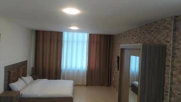 A hotel room with a bed, a wardrobe, and a large window with curtains.
