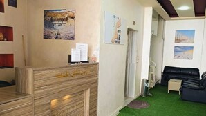 A hotel reception area with a wooden reception desk, green artificial grass flooring, and a black leather sofa in the background. - Rayan Hotel Suites (Amman)