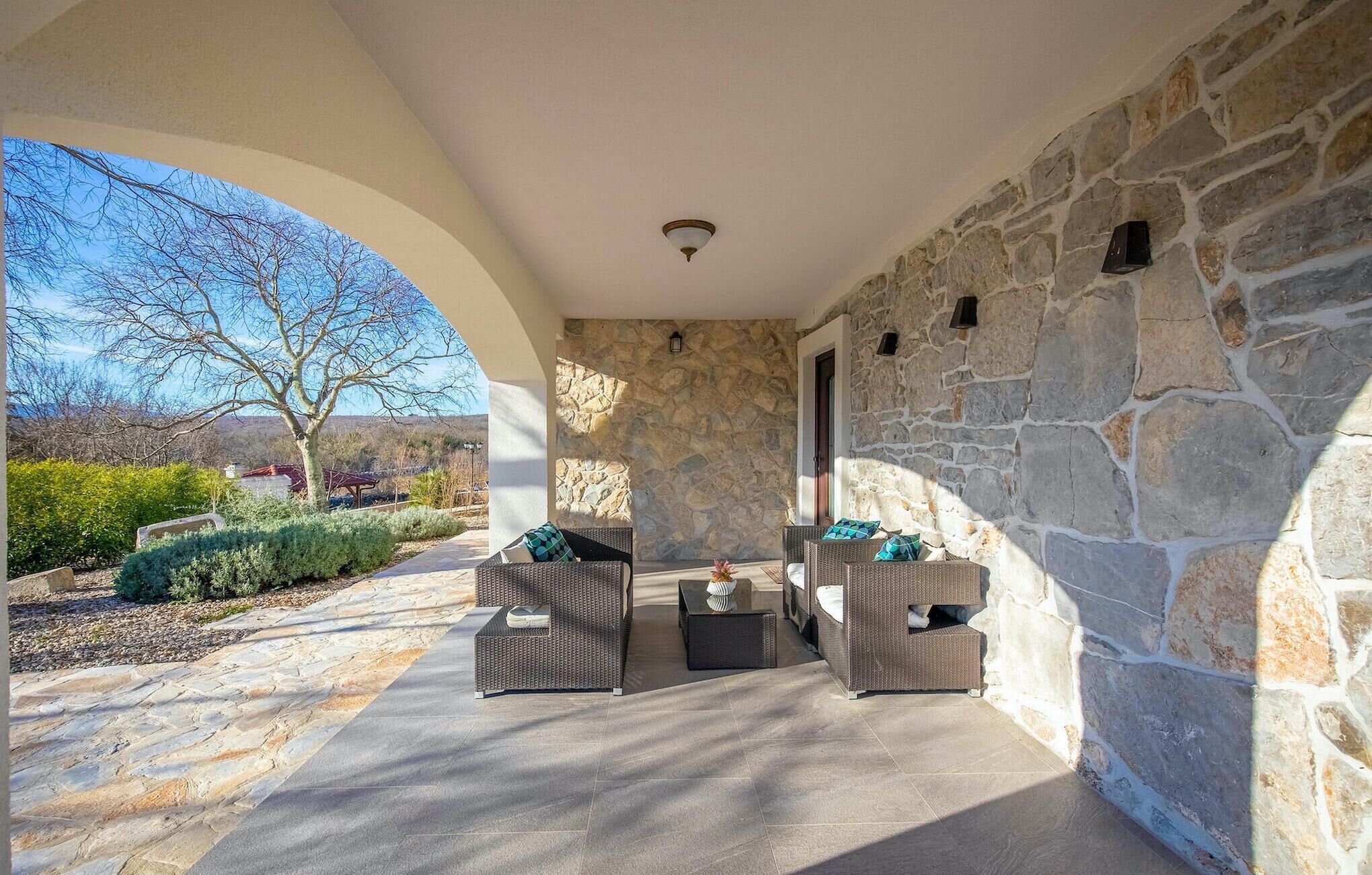 A covered patio area with stone walls, wicker furniture, and a view of the outdoors.