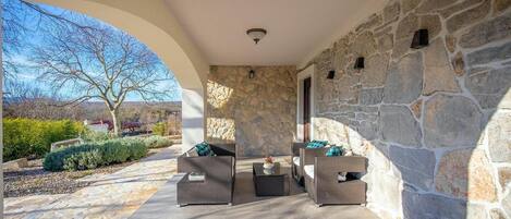 A covered patio area with stone walls, wicker furniture, and a view of the outdoors.