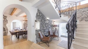 Un vaste espace dédié à la salle à manger, avec un mur en pierre, un escalier doté d’une rampe en fer forgé et une vue sur l’extérieur.