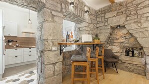 Un intérieur rustique avec des murs en pierre, une table et des chaises en bois, un coin cuisine doté de meubles blancs et une cheminée en pierre.
