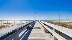 A wooden boardwalk leading to a beach with a flag in the distance. - Snowbird Availability!  Beachfront 3BR!!  Inquire for best Rates! (Orange Beach)