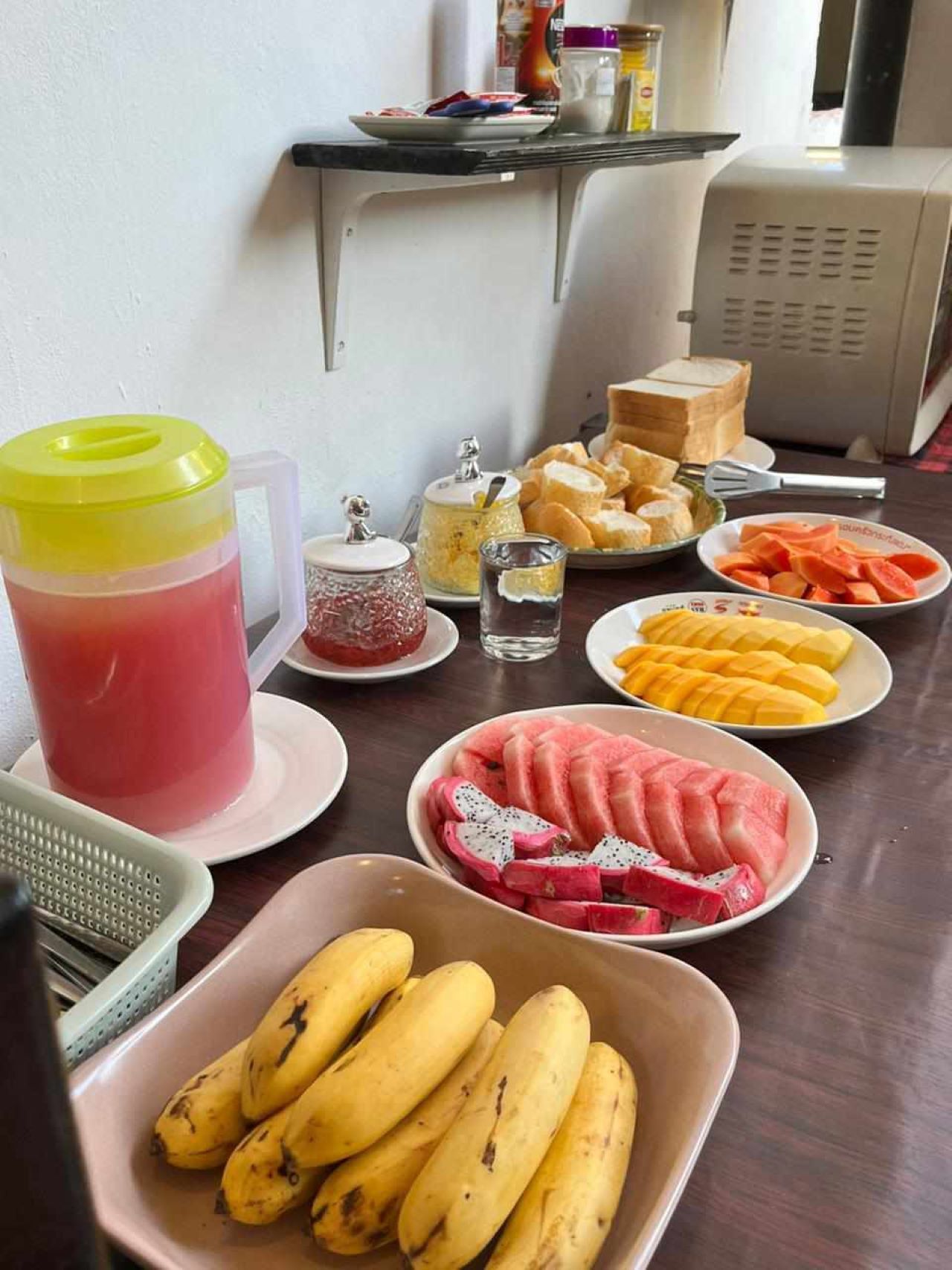 Una mesa de desayuno con varias frutas, un jarro de bebida rosa y un tostador.