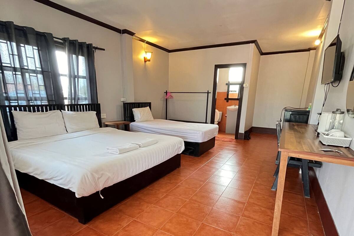 A hotel room with two beds, a wooden desk, and a bathroom visible through an open door.