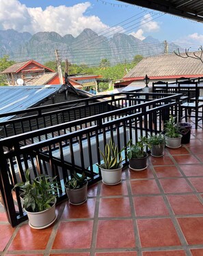 Un balcon agrémenté de plantes en pot, un sol carrelé et une vue sur les montagnes en arrière-plan.