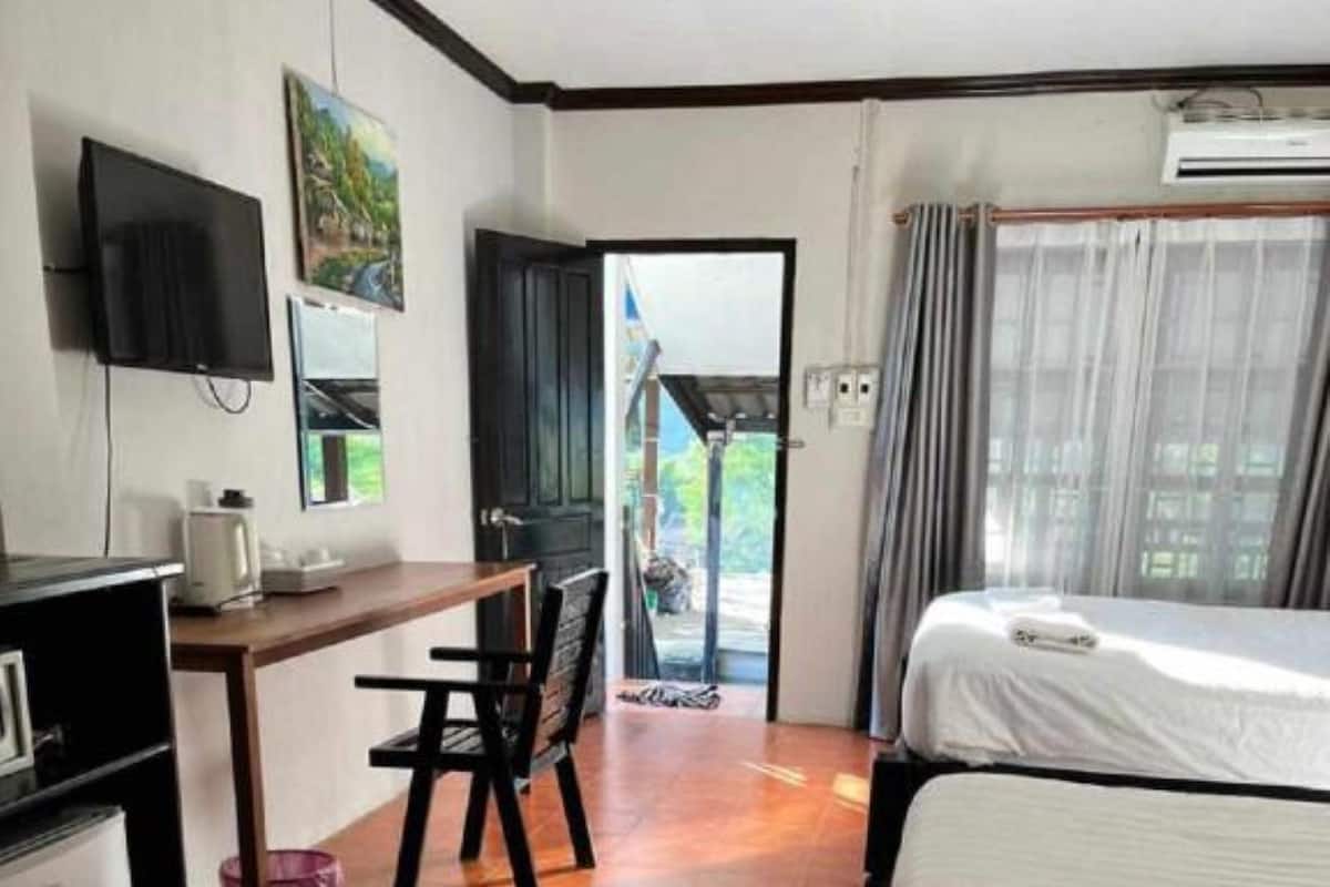 A hotel room with two beds, a desk with a chair, a TV mounted on the wall, and a window with curtains.