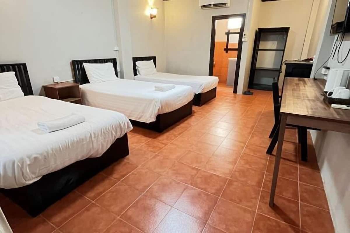 A hotel room with three beds, a wooden table, a chair, and a small desk with a computer.