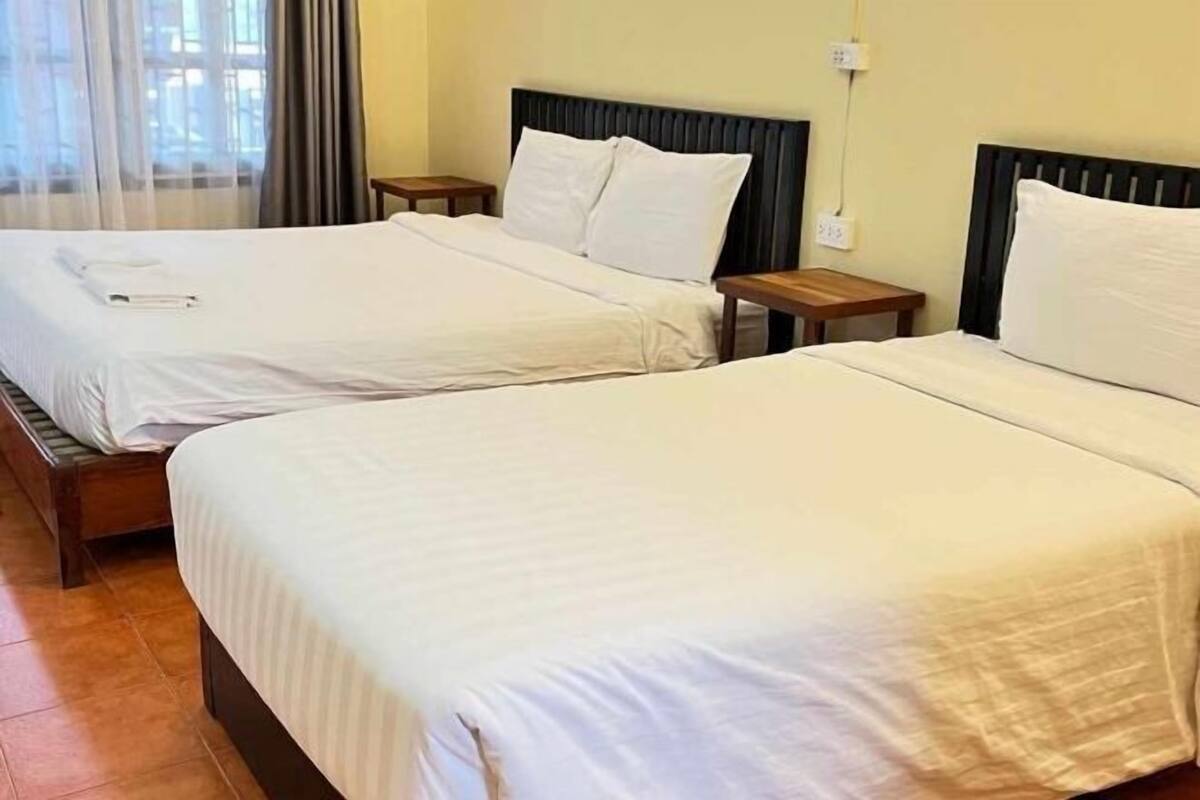 Two single beds with wooden headboards, a bedside table, and a power outlet on the wall.