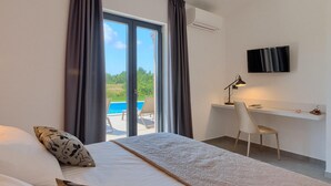 Un dormitorio con cama, escritorio, silla, televisor y vista a una piscina.