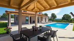Un espacio al aire libre techado con piscina, sillas de descanso y una mesa de comedor.