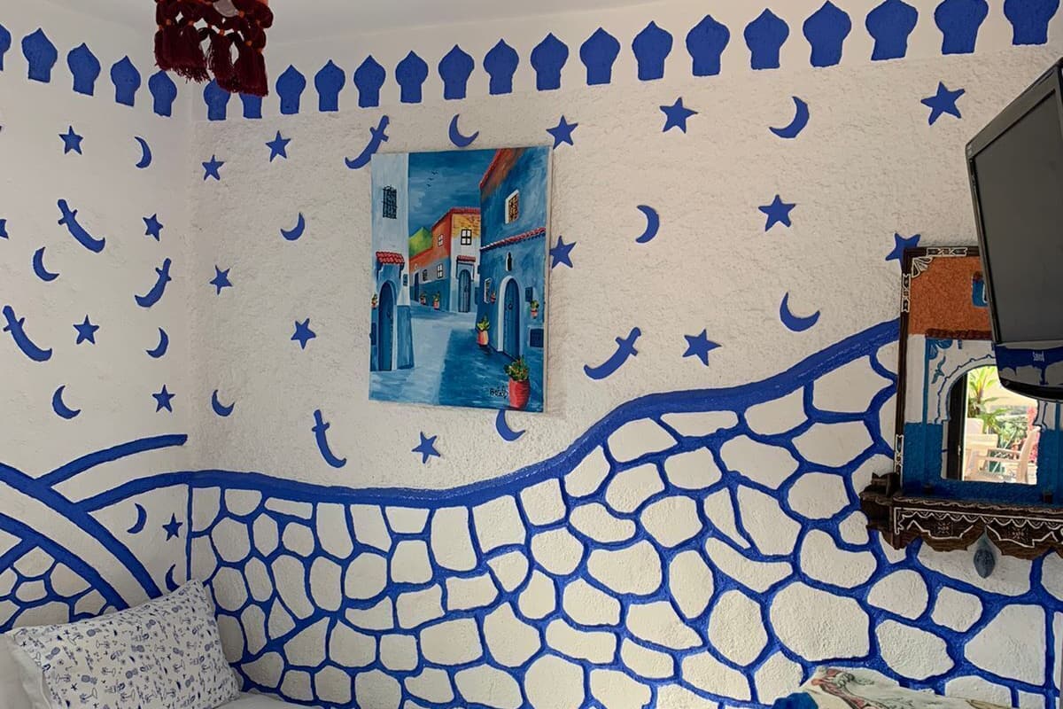 Ein Zimmer mit einer weißen Couch, einem Gemälde einer blauen Straßenszene, einer Wand mit blau-weißen Mustern und einem kleinen Tisch mit einem Korb.