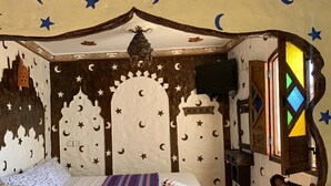 Une chambre à coucher comprenant un lit, une table de chevet, un téléviseur et une fenêtre ornée d’un motif géométrique.