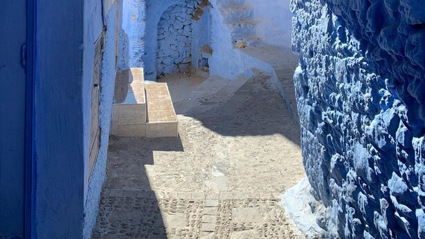 Une ruelle étroite, surmontée d’une arche peinte en bleu, qui mène à une cour intérieure.