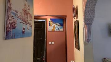 A hallway with a door leading to a room, decorated with two paintings and a patterned wall.