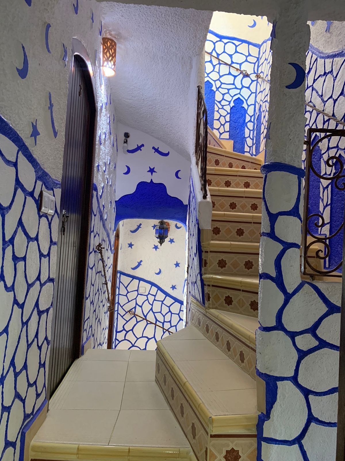 A staircase with blue and white patterned walls, a handrail, and a door at the top.