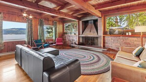 Interior acogedor de una cabaña con chimenea, sofás de cuero y un amplio ventanal con vistas panorámicas.