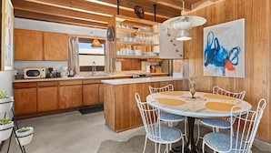 Eine moderne Küche mit Holzschränken, einer Kochinsel und einem Essbereich mit rundem Tisch und Stühlen.