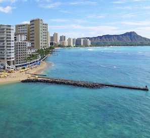 Un paysage urbain côtier avec une plage, une eau d’un bleu limpide et une montagne en arrière-plan.