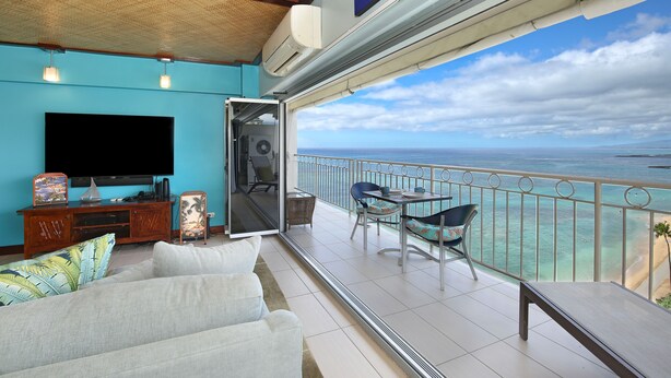 Een woonkamer met een grote televisie, een bank en een balkon met uitzicht op zee.