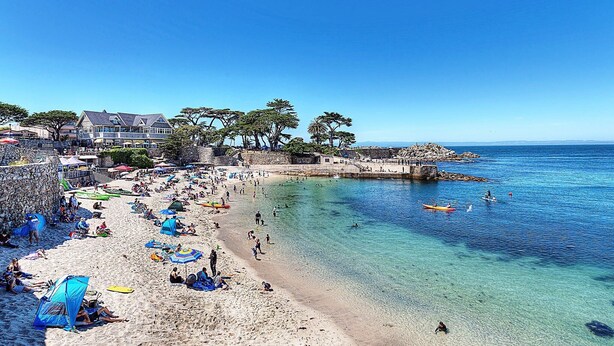 Una platja amb aigües clares, ombrel·les i gent.