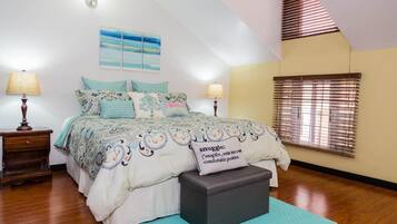 Una camera da letto con un letto, due abat-jour, una finestra con persiane, un quadro appeso al muro e un soffitto a falde.