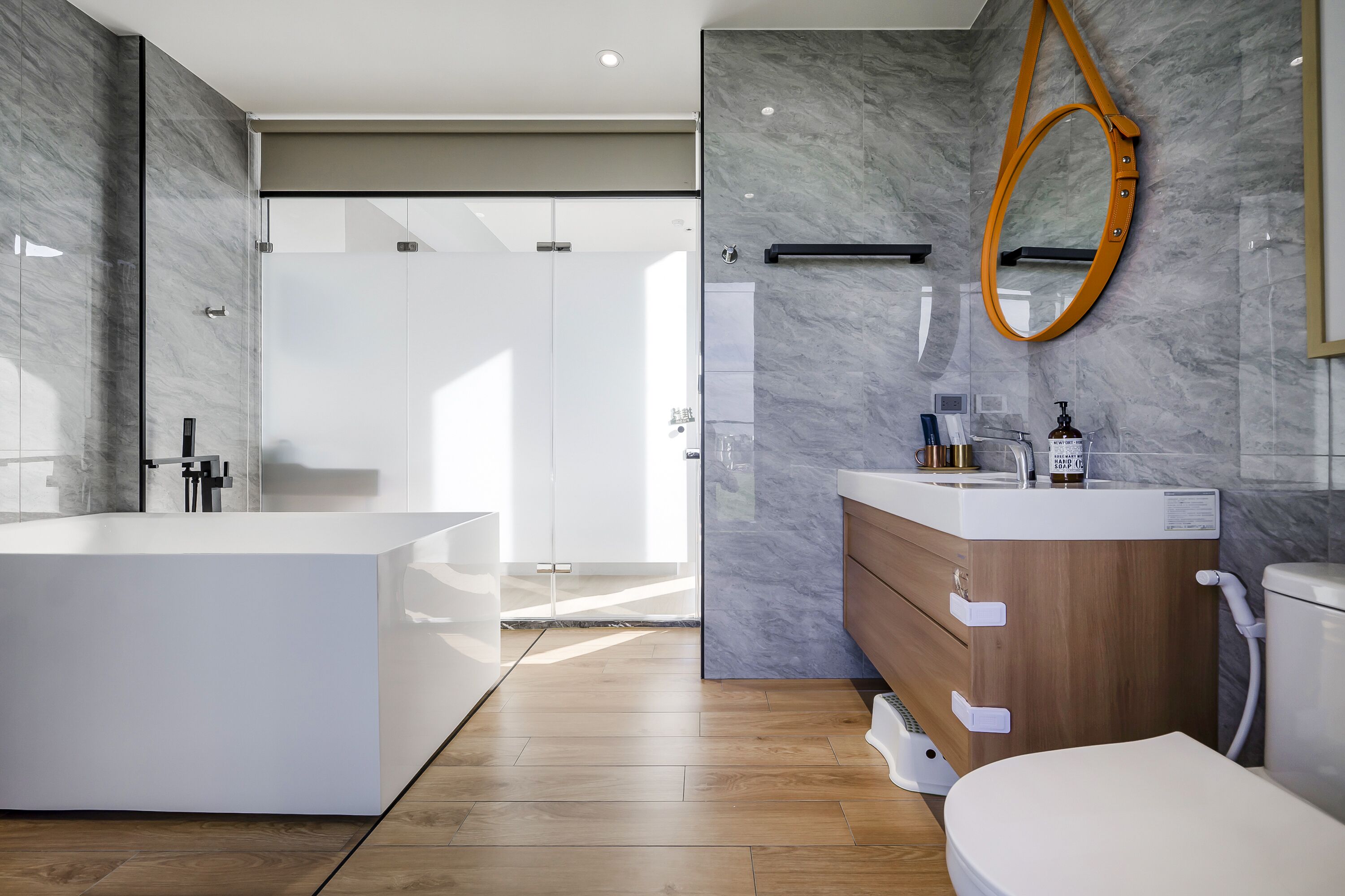 Et moderne badeværelse med et stort badekar, et trækommode og en brusekabine i glas.