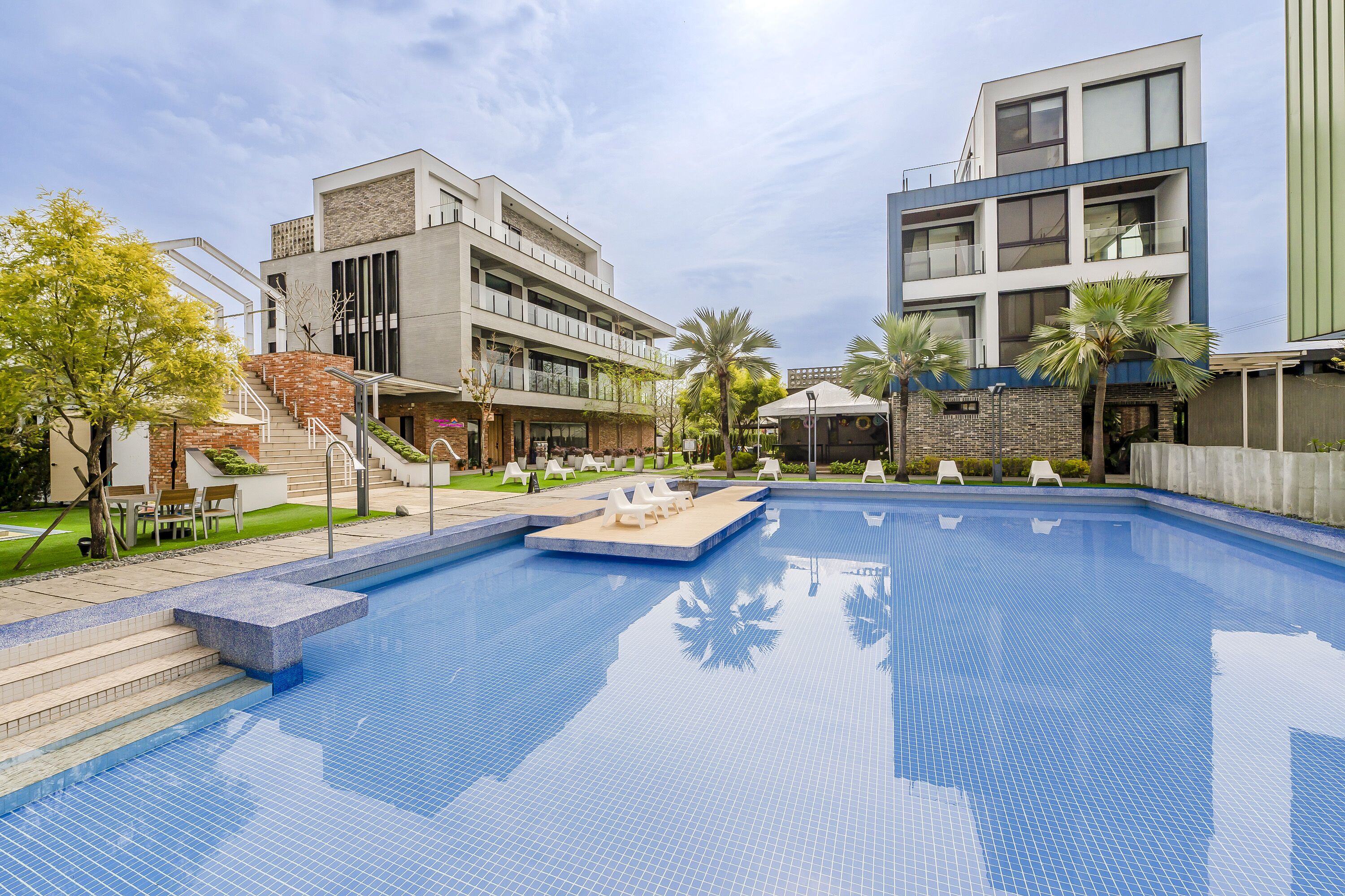 A modern hotel with a swimming pool, outdoor seating, and a staircase leading to the entrance.