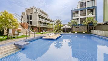 A modern hotel with a swimming pool, outdoor seating, and a staircase leading to the entrance.