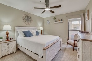 A bedroom with a bed, nightstand, dresser, chair, ceiling fan, window, and decorative wall piece. - Lake Havasu City Condo: 1 Mi to Boat Ramp! (Lake Havasu City)