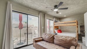 Ein Zimmer mit einer Schlafcouch, einem Etagenbett, einem Deckenventilator und großen Fenstern.