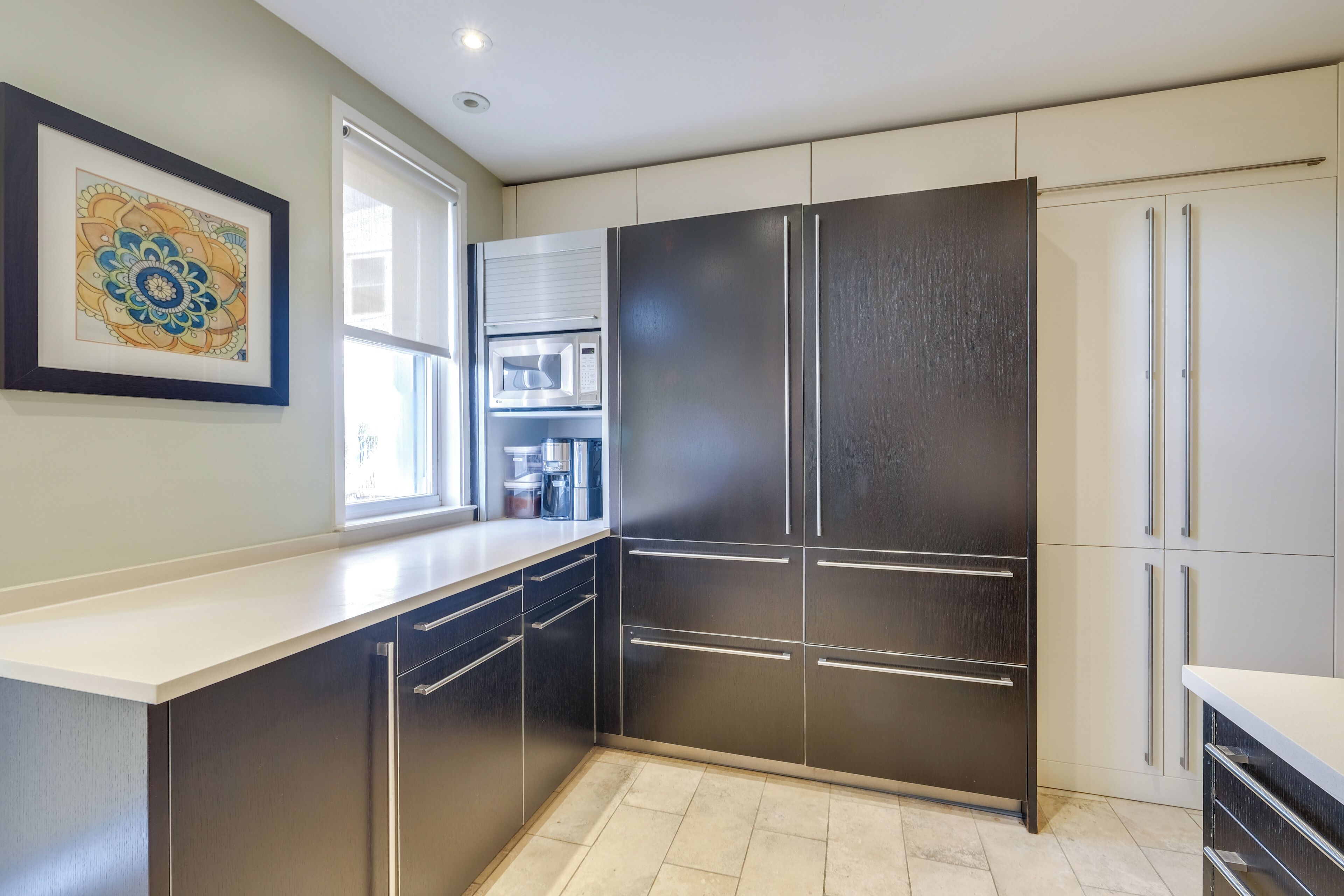 A modern kitchen with stainless steel appliances, a large refrigerator, and a window providing natural light.